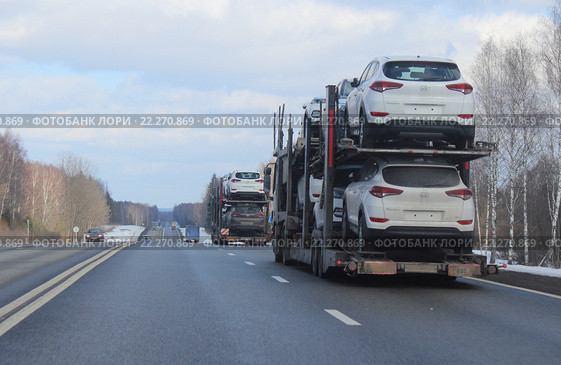 Автовозы с новыми белыми автомобилями на дороге зимой на фоне голубого неба. Car transporter (carriers) with new white cars on the road in winter against the blue sky. (2016 год). Редакционное фото, фотограф Илья Илмарин / Фотобанк Лори