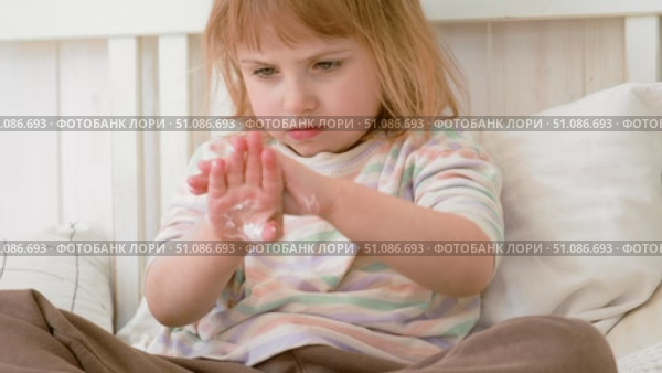 Baby girl finger applying moisturizing cream on her hand in white bedroom. Child puts lotion on hands. Skin care. Clean smooth body skin. Skincare, wellness, hygiene. Soft natural light, low contrast. Стоковое видео, видеограф Марина Демидюк / Фотобанк Лори