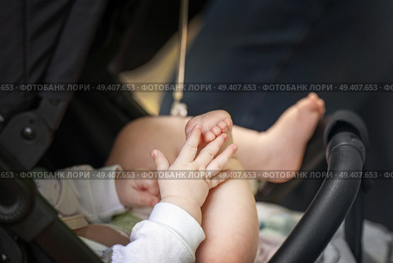 Baby in stroller demonstrates early development stage - hand-foot interaction, a precursor to crawling. Стоковое фото, фотограф Татьяна Степанищева / Фотобанк Лори
