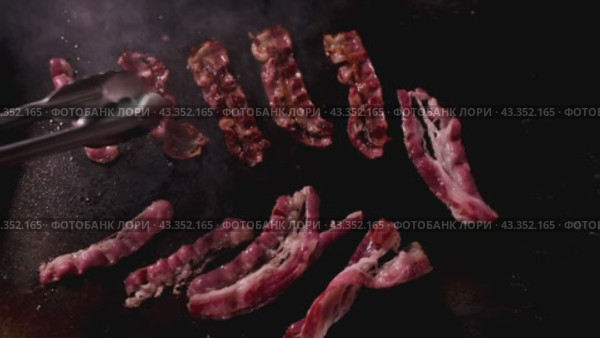 Bacon sizzling on a hot griddle, creating a delightful aroma and crispy texture. Стоковое видео, видеограф Victor Kaprov / Фотобанк Лори