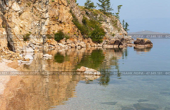 Baikal Lake in summer. Sandy beach in shallow bay of Olkhon Islands and transparent clear blue water wit reflection on coastal rocks on July morning. Scenic lakeside landscape. Natiral background. Стоковое фото, фотограф Виктория Катьянова / Фотобанк Лори