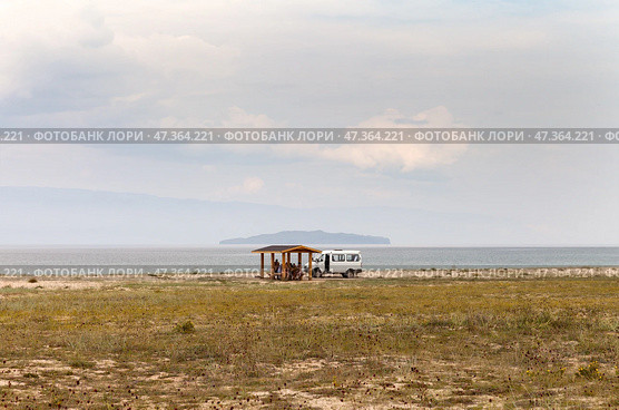 BAIKAL LAKE, KHUZHIR VILLAGE, IRKUTSK REGION, RUSSIA - August 01, 2024: Pribaikalsky Nature Park. A group of tourists have lunch in cozy wooden gazebo on shore of Small Sea on hot summer day. Редакционное фото, фотограф Виктория Катьянова / Фотобанк Лори