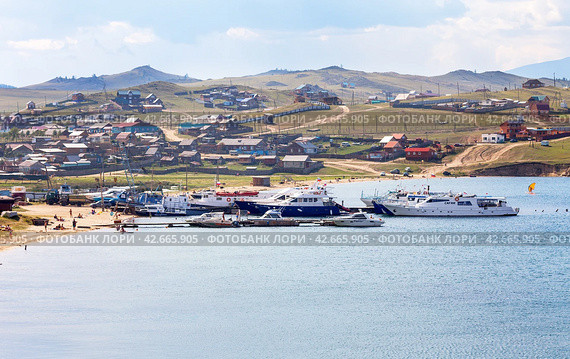 BAIKAL LAKE, OLKHON ISLAND, SAKHYURTA VILLAGE, IRKUTSK REGION, RUSSIA - August 14, 2023: Top view of Sakhyurta village with tourist houses on shore and pleasure ships on pier on summer day. Редакционное фото, фотограф Виктория Катьянова / Фотобанк Лори