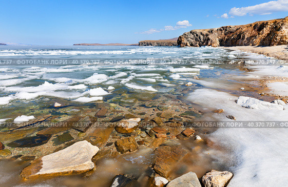 Baikal Lake on sunny May day. Melting ice on beach of Olkhon Island. Through thawed patches with clear water one can see stones at bottom of bay. Picturesque spring landscape. Spring hiking, travel. Стоковое фото, фотограф Виктория Катьянова / Фотобанк Лори