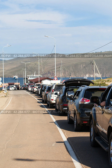 BAIKAL LAKE, SAKHYURTA VILLAGE, IRKUTSK REGION, RUSSIA - August 14, 2023: Traditional summer queue of tourist cars for the ferry crossing to Olkhon Island - popular holiday destination. Редакционное фото, фотограф Виктория Катьянова / Фотобанк Лори