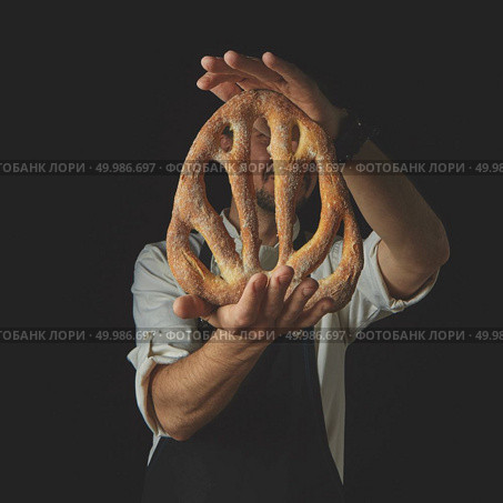 Baker holding fresh organic fougas bread on a dark background. Baker holding fougas bread. Стоковое фото, агентство Ingram Publishing / Фотобанк Лори