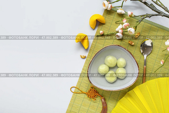Бамбуковый коврик с миской таньюаней, китайским декором и сакурой на белом фоне. Праздник Дунцзы. Стоковое фото, фотограф Pixel_shot / Фотобанк Лори
