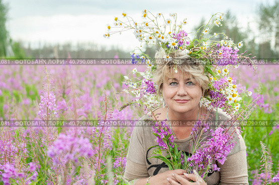 Beautiful 60s mid mature woman at nature in a a wreath of flowers in hair. Gorgeous looking old happy lady smiling. Summertime vibe. Peace and harmony. Healthy skin care. Стоковое фото, фотограф Оксана Медведева / Фотобанк Лори
