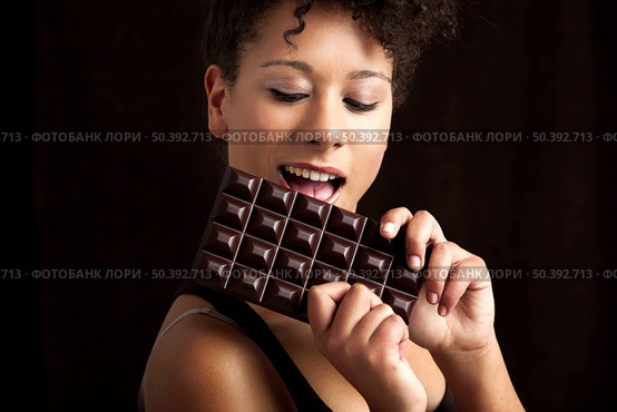 Beautiful african woman holding and eating a huge dark chocolate bar. Стоковое фото, агентство Ingram Publishing / Фотобанк Лори