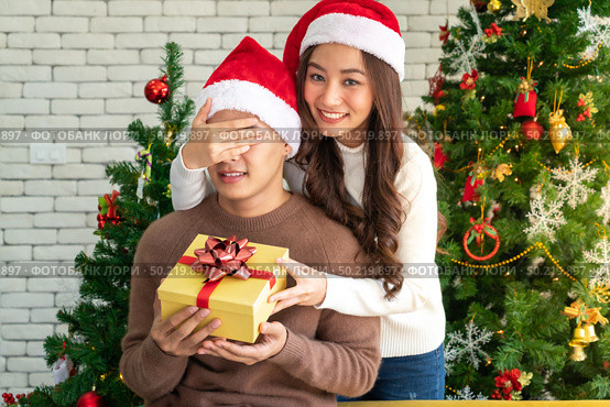 beautiful asian girl give surprise christmas gift to her boyfriend in Christmas holiday season greeting. Стоковое фото, агентство Ingram Publishing / Фотобанк Лори