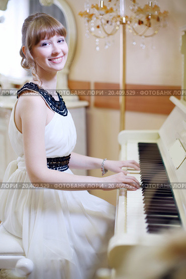 Beautiful girl in white dress plays white piano and looks at camera in light room. Стоковое фото, фотограф Losevsky Pavel / Фотобанк Лори