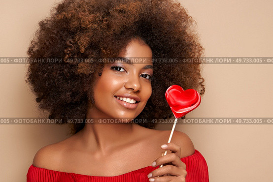 Beautiful portrait of an African girl with a heart shaped lollipop. Valentine’s Day. Symbol of love. Стоковое фото, агентство Ingram Publishing / Фотобанк Лори