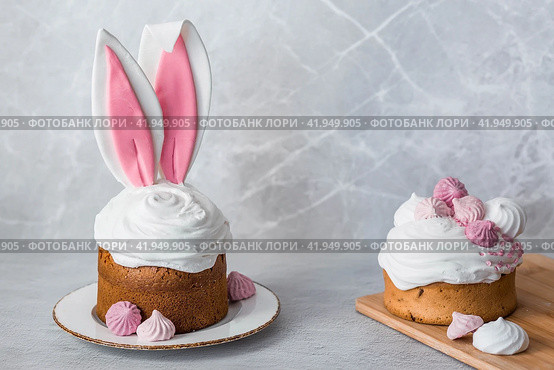 Beautiful stylish still life. Easter cake with rabbit (hare) ears, meringue, marshmallows, Easter eggs and willow branches and on a light concrete background. Happy Easter 2024. (2023 год). Стоковое фото, фотограф Photojuli / Фотобанк Лори