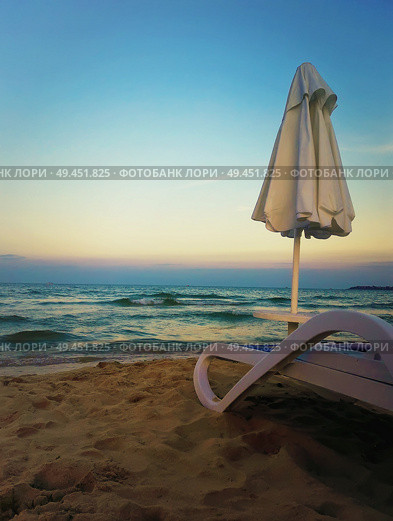 Beautiful sunset view as a deckchair with umbrella on the sand beach in front of a blue sea water. Стоковое фото, агентство Ingram Publishing / Фотобанк Лори