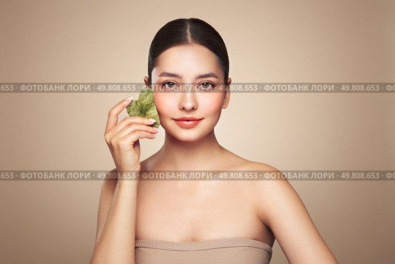 Beauty young woman doing skin care routine, scrapping, massage facial skin with jade gua sha scrapper, Facial treatment for anti aging and cosmetic cleaning. Стоковое фото, агентство Ingram Publishing / Фотобанк Лори