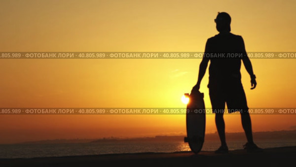 Black silhouette of a man standing near the ocean holding a longboard at bright orange sunset. Стоковое видео, видеограф Константин Шишкин / Фотобанк Лори