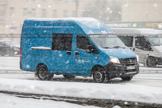 Blue cargo van drive during snowfall. Minibus moving on city road in blizzard at winter. Редакционное фото, фотограф Константин Григорьев / Фотобанк Лори