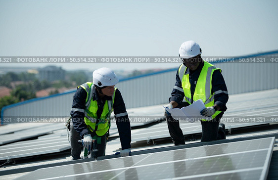 Both of Engineer in charge of solar panel installation The installation of solar energy conversion into electricity for a warehouse is currently being investigated. Стоковое фото, агентство Ingram Publishing / Фотобанк Лори