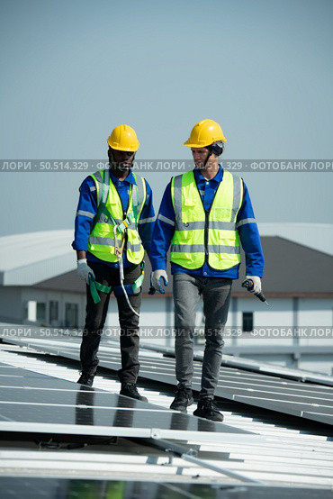 Both of Engineer in charge of solar panel installation The installation of solar energy conversion into electricity for a warehouse is currently being investigated. Стоковое фото, агентство Ingram Publishing / Фотобанк Лори