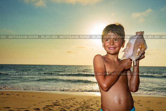 Boy listen to huge seashell over sea, sunset sun. Стоковое фото, фотограф Сергей Новиков / Фотобанк Лори