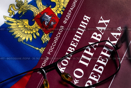 Брошюра с конвенцией "О правах ребенка" на фоне флага Российской Федерации лежит на столе (2023 год). Редакционное фото, фотограф Николай Винокуров / Фотобанк Лори