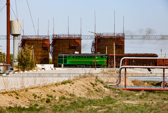 Brown rusted old oil storage tanks under bright sun on blue sky. Railway terminal of refinery plant in desert. Locomotive and carriages. Taraz city, Kazakhstan. Стоковое фото, фотограф Alexey Rezvykh / Фотобанк Лори