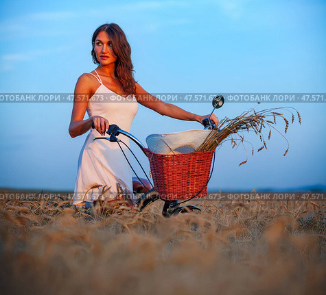Brunette woman in white dress with bicycle in wheat field at sunset. Стоковое фото, фотограф Nobilior / Фотобанк Лори