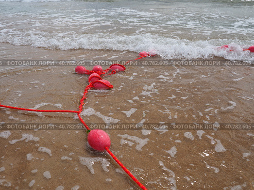 Buoys on a rope in sea water. The lifebuoys are pink restraints to alert people to the depth of the water. Rescue of the drowning. Delimiting a place on sandy beach between hotels. Wave with bubbles. Стоковое фото, фотограф Юлия Петровская / Фотобанк Лори