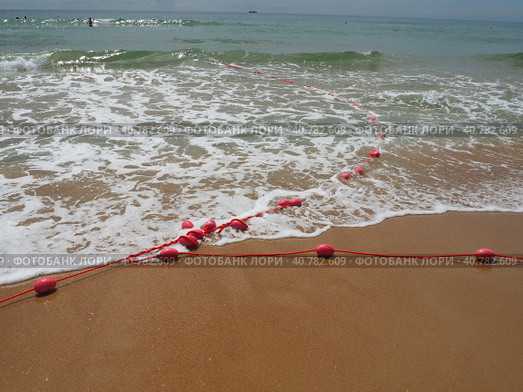 Buoys on a rope in sea water. The lifebuoys are pink restraints to alert people to the depth of the water. Rescue of the drowning. Delimiting a place on sandy beach between hotels. Wave with bubbles. Стоковое фото, фотограф Юлия Петровская / Фотобанк Лори