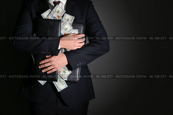 Businessman holding briefcase with dollar banknotes on dark background. Corruption concept. Стоковое фото, фотограф Pixel_shot / Фотобанк Лори