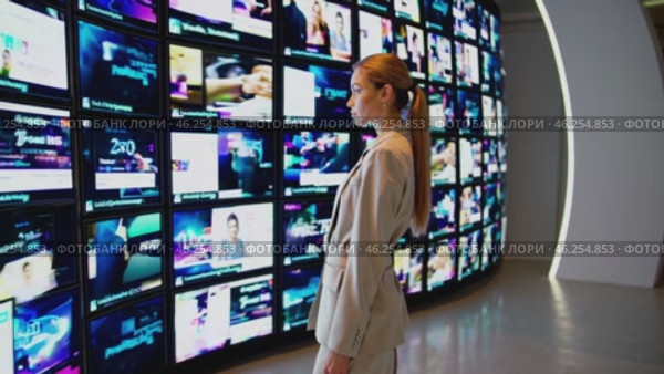 Businesswoman looking at multiple tv screens showing different multimedia content. Стоковое видео, видеограф Данил Руденко / Фотобанк Лори