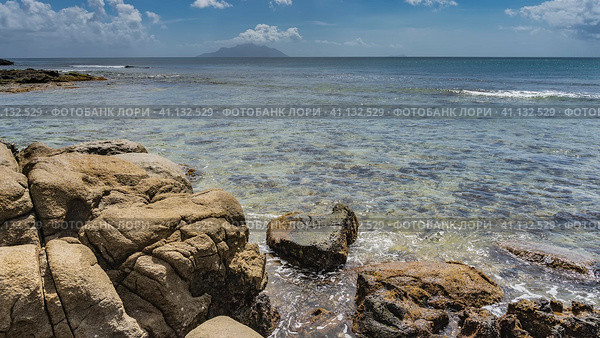 Calm seascape. Endless ocean with clear turquoise water. The outline of the island on the horizon. Blue sky, clouds. In the foreground - picturesque cracked smoothed boulders. Seychelles. Стоковое фото, фотограф Вера Ивановна Кубарева / Фотобанк Лори