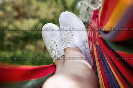 Camping in nature. Women's feet, shod in white sneakers, on a hammock in the summer garden. The concept of a carefree summer vacation. Стоковое фото, фотограф Photojuli / Фотобанк Лори