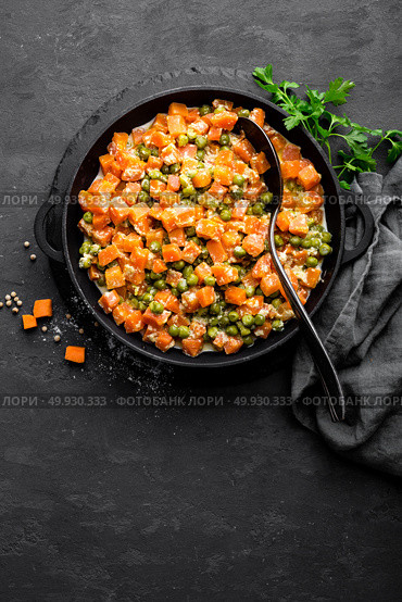 Carrot braised with fresh green peas in creamy milk sauce in stewpan, vegetable saute on black background, top view. Стоковое фото, агентство Ingram Publishing / Фотобанк Лори