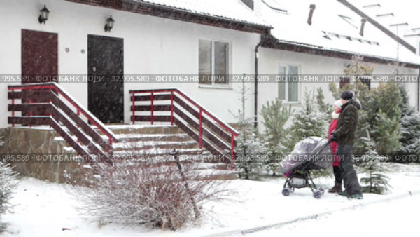 Caucasian loving couple coming to townhouse porch and entrance with baby stroller after waling. Strong snowfall at winter. Стоковое видео, видеограф Кекяляйнен Андрей / Фотобанк Лори