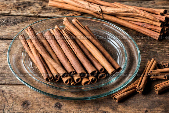 Ceylon cinnamon sticks in glass plate on wooden board, rustic style. Still life natural food of sri lankan cinnamon sticks on table at grey wall. Delicious tasty healthy concept. Copy ad text space. Стоковое AI-изображение, AI-художник Aleksandr Golubev / Фотобанк Лори
