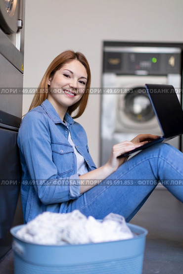 cheerful woman uses laptop computer waiting at the laundrette. Стоковое фото, агентство Ingram Publishing / Фотобанк Лори