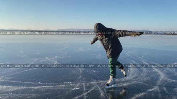 Человек катается на коньках на замёрзшем озере с прозрачным льдом в ясный солнечный морозный день. Редакционное видео, видеограф Светлана Акифьева / Фотобанк Лори