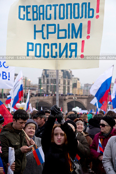 Человек с плакатом "Севастополь! Крым! Россия" участвует в многотысячном митинге-концерте на Красной площади в поддержку референдума о вхождении Крыма в состав России (2014 год). Редакционное фото, фотограф Николай Винокуров / Фотобанк Лори