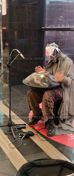 Человек в голографической маске играет мелодию на музыкальном инструменте ханг в метро в переходе. Редакционное фото, фотограф Светлана Русских / Фотобанк Лори