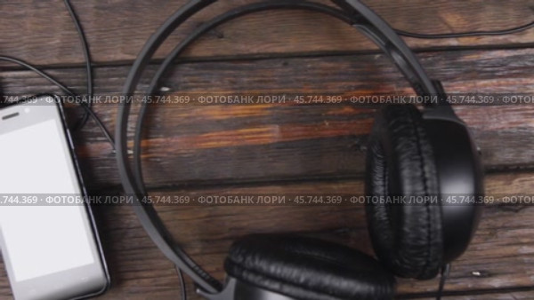 Черные наушники и смартфон на деревянном столе. Снимок с журавля. Вид сверху. Телефон, дисплей, мультимедиа. Стоковое видео, видеограф Александр Собко / Фотобанк Лори
