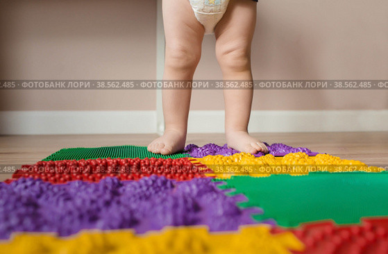 Child feet on orthopedic baby massage puzzle floor mats with colorful details for preventing flatfoot. Стоковое фото, фотограф Photojuli / Фотобанк Лори