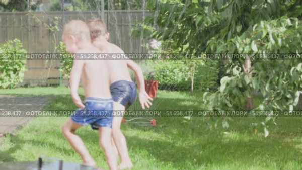 Children joyfully playing in a sprinkler on a warm and sunny summer day outside. Стоковое видео, видеограф Olesia Kondrateva / Фотобанк Лори