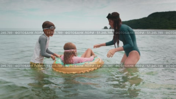 Childs enjoy time in shallow sea water, playing with float ring. Scene captures bonding family, joy and outdoor fun. Happy family moment during summer vacation, filled with laughter and love. Стоковое видео, видеограф Енваев Андрей / Фотобанк Лори