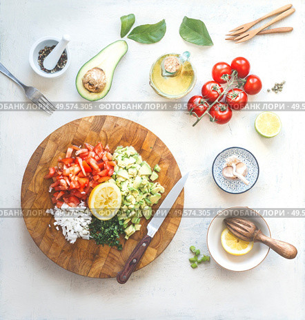 Chopped ingredients for avocado salsa, guacamole  or salad on cutting board. Fresh cut avocado, tomatoes , lemon, lime , olives oil, garlic and chili a on white kitchen table. Top view. Стоковое фото, агентство Ingram Publishing / Фотобанк Лори