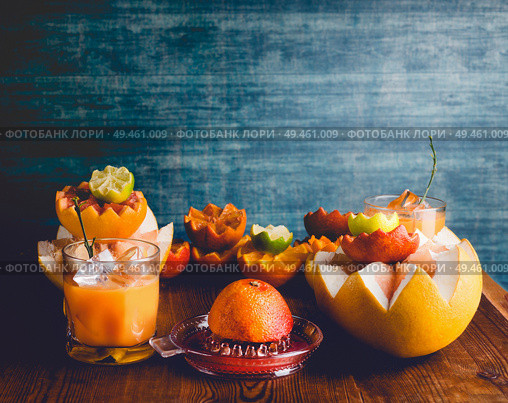 Citrus juice in glass and citrus squeezer on table with various tropical citrus fruits at dark wall background. Vitamin C. Healthy drinks. Grapefruit, orange, tangerine, lemon, lime and pomelo. Стоковое фото, агентство Ingram Publishing / Фотобанк Лори