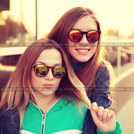 Close up fashion portrait of two young hipster girl friends, wearing mirrored sunglasses, having blonde and ombre hairs. Стоковое фото, агентство Ingram Publishing / Фотобанк Лори