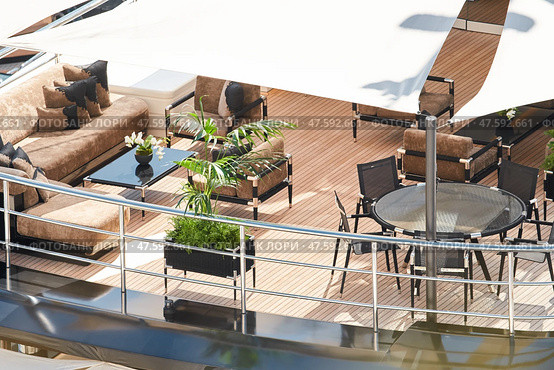 Close up footage of a relaxation area on the open teak deck of an expensive megayacht at sunny day, with awnings stretched over the deck to protect from the sun, wealth life, table and chairs. Стоковое фото, фотограф Vladimir Drozdin / Фотобанк Лори