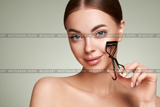 Close up of a beautiful young woman curling her eyelashes. Eyelash extensions. Стоковое фото, агентство Ingram Publishing / Фотобанк Лори