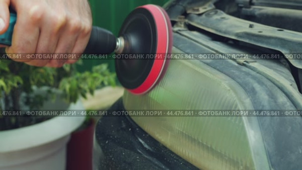 Close-up of a hand holding a drill and polishing a car headlight. The headlight is dull. Polishing with a black and red felt disc. Стоковое видео, видеограф Воловодов Владимир / Фотобанк Лори